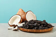 Front view photography at a rattan tray of black locust fruit and some coconuts placed side by side on table against blue background. Blank space for adding text or elements of design
