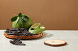 White table contains a rattan tray with black locust fruits and grapefruit above next to an empty podium for displaying product. Advertising photo with brown background and space for text