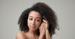 Beauty and Healthcare concept - Beautiful African American woman with curly afro hairstyle hair and clean, healthy skin on gray studio background posing and looking at camera