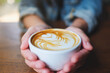 Closeup image of hands holding a cup of hot coffee with latte art