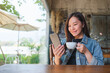 Portrait image of a young beautiful woman holding and using mobile phone while drinking coffee in cafe