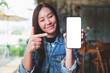 Mockup image of a young woman holding, showing and pointing finger at a mobile phone with blank white screen