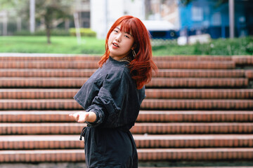 Wall Mural - Joyful Korean woman with red hair dancing against an urban backdrop