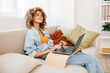 Smiling woman sitting on a cozy sofa, typing on her laptop in a modern living room