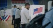 © Framestock - Elderly male voter with bulletin in hands comes to voting booth. Multicultural American citizens come to vote in polling station. Political races of US presidential candidates. National Election Day.