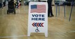 © Framestock - Vote here sign on floor. Woman with spinal muscular atrophy in electric wheelchair comes to vote in polling station. Political races of US presidential candidates. National Election Day. Dolly shot.