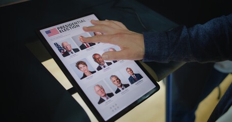 Close up of Caucasian man making choice and voting for US presidential candidate in voting booth using tablet computer. US citizen at polling station during National Election Day in the United States.