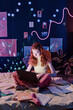 © AnnaStills - Vertical shot of modern teen girl sitting on bed using laptop while doing homework late in evening, copy space