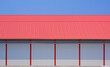 White sandwich panel wall and red metal gable roof of 2 industrial cold storage warehouse buildings against blue sky background in factory area