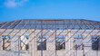 Concrete block wall with metal hip roof beam structure of incomplete modern office building in construction site against blue sky background