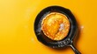 A glossy pancake lavishly coated in syrup lies in a frying pan the glossy texture highlighted by a bright yellow backdrop
