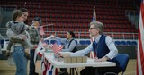 Fototapeta Kuchnia - Woman with baby on hands talks with polling officer and takes bulletin. Female American citizen comes to vote in polling station. Political races of US presidential candidates. National Election Day.