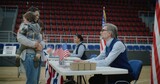 Fototapeta Kuchnia - Woman with baby on hands talks with polling officer and takes bulletin. Female American citizen comes to vote in polling station. Political races of US presidential candidates. National Election Day.
