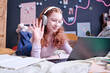 Modern teen schoolgirl wearing headphones having online class greeting her teacher on video call on laptop, copy space