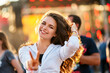 © artiemedvedev - Happy young woman enjoys summer music fest on beach with sunset backlighting. Casual outfit, dancing on sand, joyous mood, crowd blur in background, reaching out to camera for an inviting vibe.