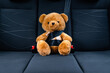 Children car safety concept. Teddy bear toy with fastened seat belt in the car traveling.