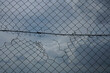 Looking up at a chain link fence with blue sky and clouds. wire fence. Chain link fence see blue sky. iron frame.