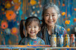 Asian grandmother and granddaughter playing with colorful paints on a table, smiling in a moment of creative joy. Family bonding and early childhood education concept