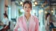 A photo of a young Asian woman in a pink suit standing in an office, looking at the camera with a serious expression.