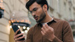 Close up upset unhappy Indian Arabian ethnic man young guy businessman male using looking mobile phone bad connection losing fortune loss fail touch head why negative result outdoors city urban street