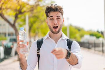 Wall Mural - Young handsome man with a bottle of water at outdoors surprised and pointing front