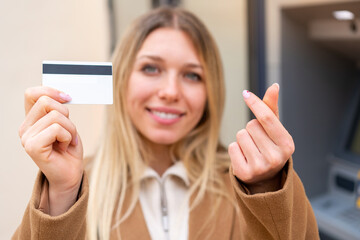 Wall Mural - Young pretty blonde woman holding a credit card at outdoors