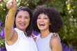 Mature biracial mother points, young daughter smiles beside her in garden