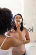 Mature biracial mother and daughter applying facial masks at home in the bathroom