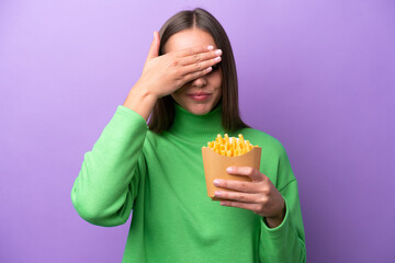 Wall Mural - Young caucasian woman holding fried chips on purple background covering eyes by hands. Do not want to see something