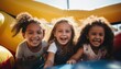 © Anna - Three young girls happily sit inside a vibrant bouncy house at a theme park, enjoying the fun and excitement
