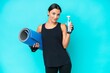 Young caucasian woman isolated on blue background with sports water bottle and with a mat