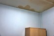 A corner of a room with a brown stain on the ceiling. The stain is likely from a leak or water damage