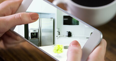 Wall Mural - Image of person using smartphone with house kitchen interiors displayed on screen