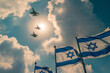 photograph of Israeli flags flying in the wind with fighter jets flying overhead against a sky background. 