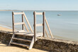 Accès à une plage par un escalier en bois enjambant un muret en pierres, devant une large baie sableuse