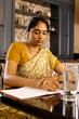 © Wavebreak Media - Indian young woman wearing traditional saree writing in notebook at home
