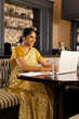 © Wavebreak Media - Indian young woman wearing traditional yellow clothing, working on laptop at home
