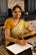 © Wavebreak Media - Indian young woman in traditional yellow saree, writing in notebook at home
