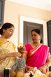 © Wavebreak Media - Indian mother and teenage daughter wearing traditional clothes, examining jar at home