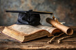 A black graduation cap sitting on top of an open book. A brown scroll lies besides it