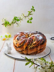 Wall Mural - A twisted yeast cake with poppy filling, powdered sugar and multi -colored sugar decor on a ceramic board on a light wooden background. Christmas and Easter pastries.