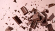 Broken chocolate bar pieces falling on pink beige background