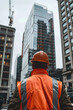 © sommersby - A man stands wearing an orange safety vest and hard hat, ready for work in a construction or industrial setting