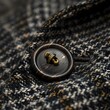 Close-up view of a polished button on a textured woolen coat, highlighting the details of quality garment craftsmanship.