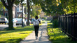Photo of an African American boy in black pants and white backpack running down the sidewalk towards school. green grass on both sides of him with some trees and buildings in background