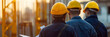 © Prasanth - team of cladding engineers dresssed in dark blue , yellow helmet , back at the camera inspecting blueprints , blurry out of focus construction site camera over rhe shoulder , warm colours , sunny day,