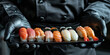 Sushi set on a black square plate. A sushi man in a suit and gloves holds a tray with different types of seafood.