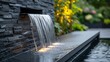 A contemporary waterfall feature with LED lighting on a black stone wall in an urban garden