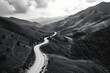 Leverage black and white drone photography to capture a dramatic perspective of a winding mountain road snaking through a lush green valley. Emphasize the scale of the landscape 