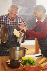 Poster - Senior man, teaching and cooking with pot for cheese or diary dish in kitchen together at old age home. Male person or team learning in hospitality with mixing ingredients, food or recipe at house